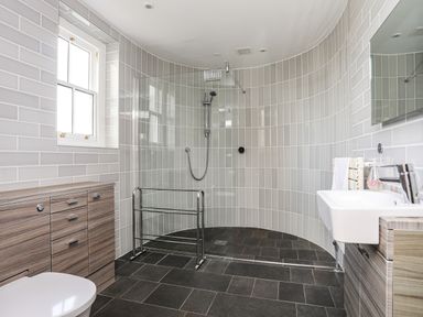 A bathroom with a walk in shower wooden cabinets a white sink and a toilet at Harlech Apartments - Branwen in Harlech
