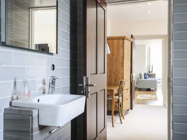 A bathroom with a sink and mirror looking into a hallway with a wooden desk chair and a living room with a sofa at Harlech Apartments - Branwen in Harlech