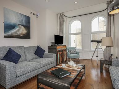 A living room with two blue sofas a wooden coffee table and a telescope near large windows at Harlech Apartments - Branwen in Harlech