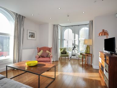 A living room with a wooden coffee table a red armchair two green chairs a telescope a wooden dresser and a flat screen TV at Harlech Apartments - Bendigeidfran in Harlech