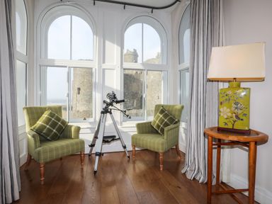 A room with two green armchairs with pillows a telescope and a wooden side table with a lamp at Harlech Apartments - Bendigeidfran in Harlech