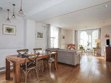 A living and dining area with wooden table and chairs sofas armchairs large arched windows and a telescope at Harlech Apartments - Bendigeidfran in Harlech