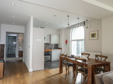 A dining area with wooden table and chairs next to a kitchen with white cabinets and tiled backsplash at Harlech Apartments - Bendigeidfran in Harlech