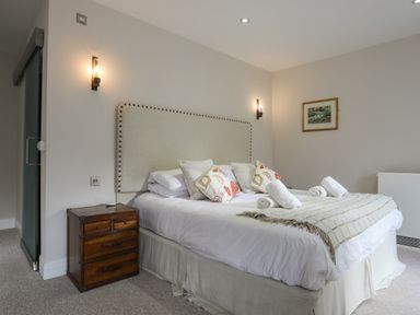 A bedroom with a bed with pillows and rolled towels on it a wooden bedside table and a framed picture on the wall at Harlech Apartments - Bendigeidfran in Harlech
