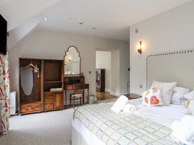 A bedroom with a bed with cushions and rolled towels a wooden wardrobe with an iron and ironing board and a wooden desk with a mirror at Harlech Apartments - Bendigeidfran in Harlech
