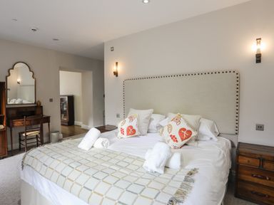 A bedroom with a large bed featuring patterned pillows and towels and wooden furniture including a desk and nightstand at Harlech Apartments - Bendigeidfran in Harlech
