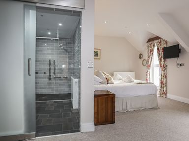 A bedroom with a bed and rolled towels next to a shower area with grey tiled walls at Harlech Apartments - Bendigeidfran in Harlech