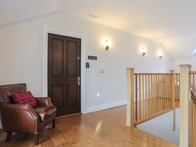 A hallway with a wooden door labeled Gwern a brown leather chair with a cushion and wooden railing at Harlech Apartments - Gwern Harlech