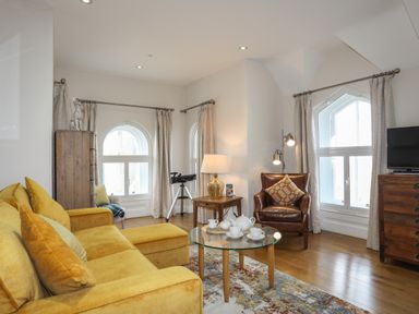 A living room with a yellow sofa a glass coffee table with tea set a brown leather chair a wooden chest of drawers and a telescope at Harlech Apartments - Gwern in Harlech