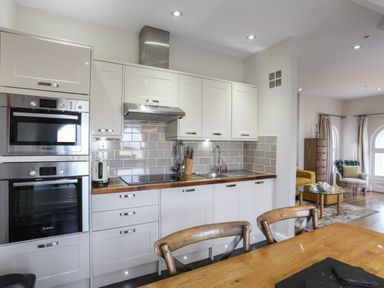 A kitchen with white cabinets, wood countertops, stainless steel oven and microwave, and a sink with a faucet at Harlech Apartments - Gwern in Harlech