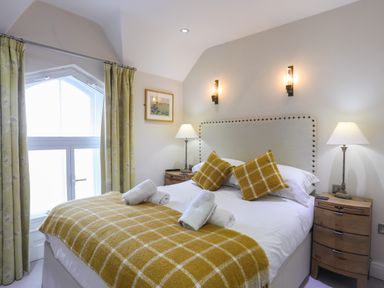 A bedroom with a bed with yellow checkered blankets and pillows next to lamps and a window with curtains at Harlech Apartments - Gwern in Harlech