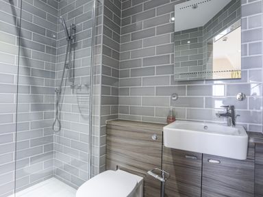 A bathroom with a shower, toilet, sink, and a mirror at Harlech Apartments - Gwern in Harlech