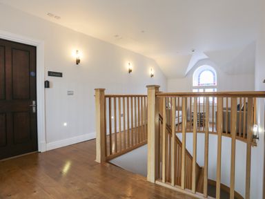 A staircase with wooden railings leading to a hallway with a dark wooden door and wall lights at Harlech Apartments - Gwern in Harlech