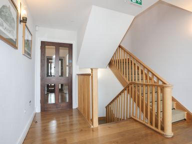 A hallway with wooden stairs and banisters with a wooden floor and framed pictures on the wall at Harlech Apartments - Gwern in Harlech