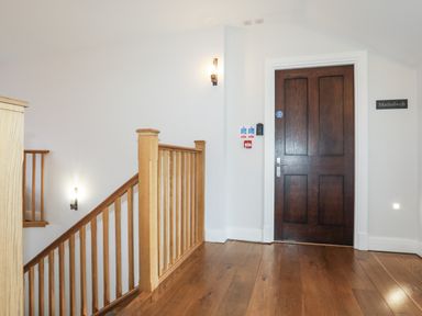 A hallway with wooden flooring a wooden staircase and a dark wooden door at Harlech Apartments - Matholwch in Harlech