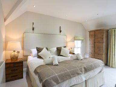 A bedroom with a large bed bedside tables with lamps a wooden wardrobe and a window at Harlech Apartments - Matholwch in Harlech