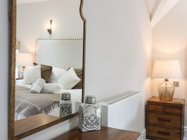 A reflection of a bed with pillows and rolled towels in a mirror next to a wooden chest of drawers with a lamp at Harlech Apartments - Matholwch in Harlech