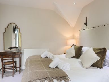 A bedroom with a bed with pillows and towels a bedside lamp and a wooden dressing table with a mirror at Harlech Apartments - Matholwch in Harlech