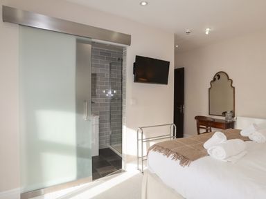 A bedroom with a bed with rolled towels a wall mounted TV a small desk with a mirror and a partially open sliding bathroom door at Harlech Apartments - Matholwch in Harlech