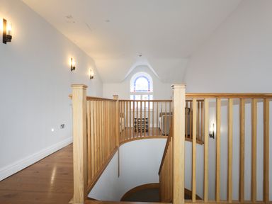 A stairway with wooden railing leading to a seating area with a window at Harlech Apartments - Matholwch in Harlech