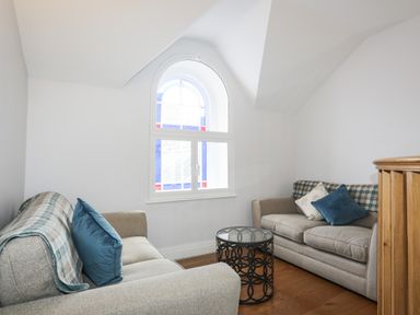 A small sitting room with two sofas and a round glass coffee table under a window with an arch at Harlech Apartments - Matholwch in Harlech