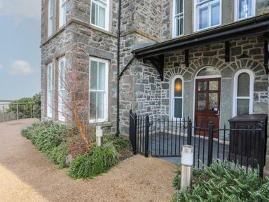 Stone building exterior with windows and wooden door gated entrance pathway and plants in Harlech Apartments Matholwch Harlech