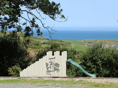 A wooden play structure with a knight on horse painting and a green slide in a grassy area with ocean and fields in the background at Hen Gilfach in Llanfairyngnhornwy