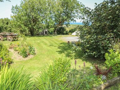 A garden with trees grass flowers a wooden wagon a play structure and a bench at Hen Gilfach in Llanfairyngnhornwy