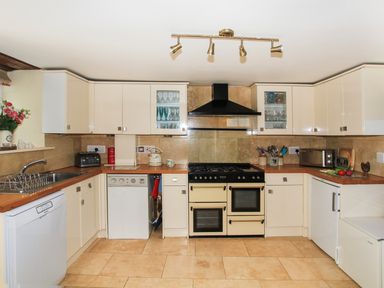 A kitchen with white cabinets a black stove a kettle a toaster a microwave and a dish drying rack at Hen Gilfach in Llanfairyngnhornwy