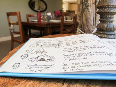 An open handwritten guestbook on a wooden table with drawings and notes in a dining room with wooden chairs and a table at Hen Gilfach in Llanfairyngnhornwy