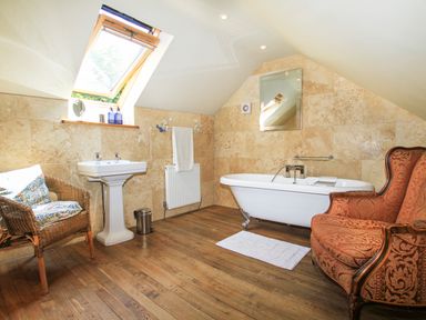 A bathroom with a clawfoot bathtub wooden floor a wicker chair and an upholstered armchair at Hen Gilfach in Llanfairyngnhornwy