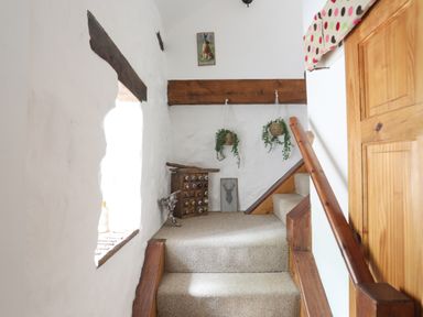 A staircase with wooden railing leading to a small landing with hanging plants and framed pictures at Hen Gilfach in Llanfairyngnhornwy