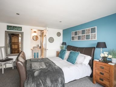 A bedroom with a brown bed, teal pillows, wooden nightstand with lamps and flowers, and a bathroom visible through an open door at Hen Gilfach in Llanfairyngnhornwy