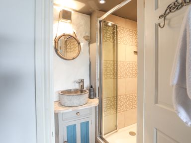A bathroom with a round mirror above a stone sink and a shower with patterned tiles at Hen Gilfach in Llanfairyngnhornwy