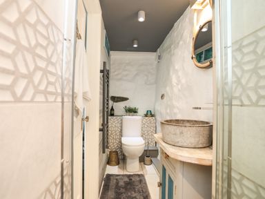 A bathroom with a toilet a stone sink a wooden cabinet a towel hanging on the door and decorative items on the tiled wall at Hen Gilfach in Llanfairyngnhornwy