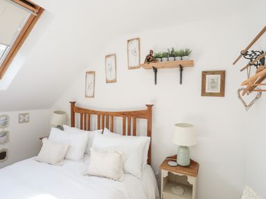 A bedroom with a wooden bed frame white bedding bedside tables lamps framed pictures and a wall shelf with plants at Hen Gilfach in Llanfairyngnhornwy