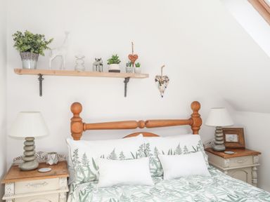 A bedroom with a wooden bed frame two bedside tables with lamps and a wooden shelf with plants and decorations at Hen Gilfach in Llanfairyngnhornwy