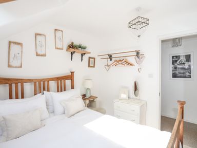 A bedroom with a wooden bed frame white bedding bedside table lamp wall art and a dresser with a mirror at Hen Gilfach in Llanfairyngnhornwy