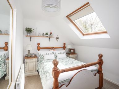 A bedroom with a wooden bed frame green leaf patterned bedding two bedside tables with lamps and a skylight window at Hen Gilfach in Llanfairyngnhornwy