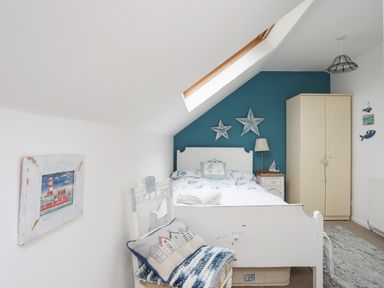 A bedroom with a white bed blue wall two star decorations a cream wardrobe and a white chair with a cushion at Hen Gilfach in Llanfairyngnhornwy