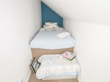 A small bedroom with a single bed a blue accent wall a small ottoman covered with a quilt and books on top at Hen Gilfach in Llanfairyngnhornwy