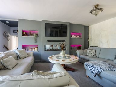 A living room with sofas a round table tv and built in shelves with pink lighting at Hen Gilfach in Llanfairyngnhornwy
