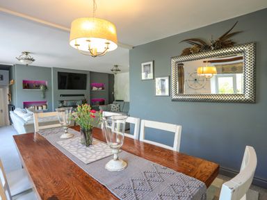 A dining table with chairs and flowers in a living room with a wall mirror and a television at Hen Gilfach in Llanfairyngnhornwy