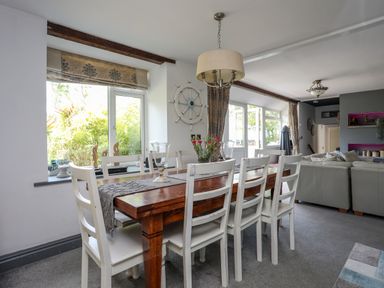 A dining area with a wooden table and white chairs next to a living room with sofas at Hen Gilfach in Llanfairyngnhornwy