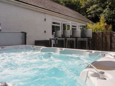 An outdoor hot tub with bubbling water next to a white building with windows and a row of bar stools at Hen Gilfach in Llanfairyngnhornwy