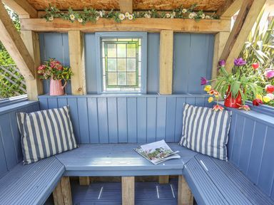 An outdoor wooden seating area with blue painted benches pillows and flowers at Hen Gilfach Stable in Llanfairyngnhornwy
