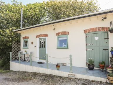 The exterior of a small building with green doors and windows and a small porch with chairs and potted plants at Hen Gilfach Stable in Llanfairyngnhornwy