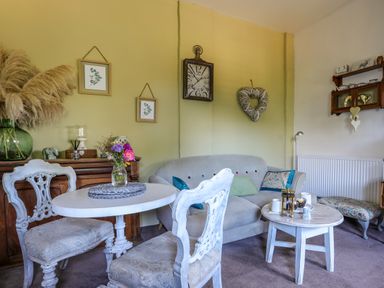 A living room with small tables and chairs a sofa and wall clock at Hen Gilfach Stable in Llanfairyngnhornwy