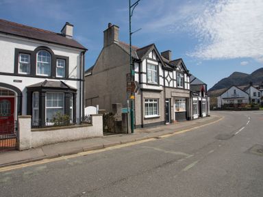 A street view with white and gray houses and a curved road with mountains in the background at Hirfron in Llanberis