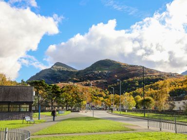 A park area with grass and benches along a road with mountains in the background at Hirfron in Llanberis